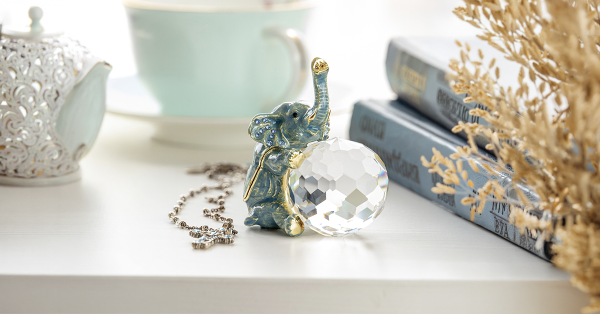 Collection of crystal animal figurines including fish and elephant displayed on white shelf with turquoise cup and jewelry