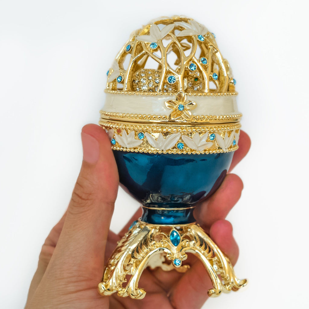 Decorative egg with gold and blue design held by a hand on a white background