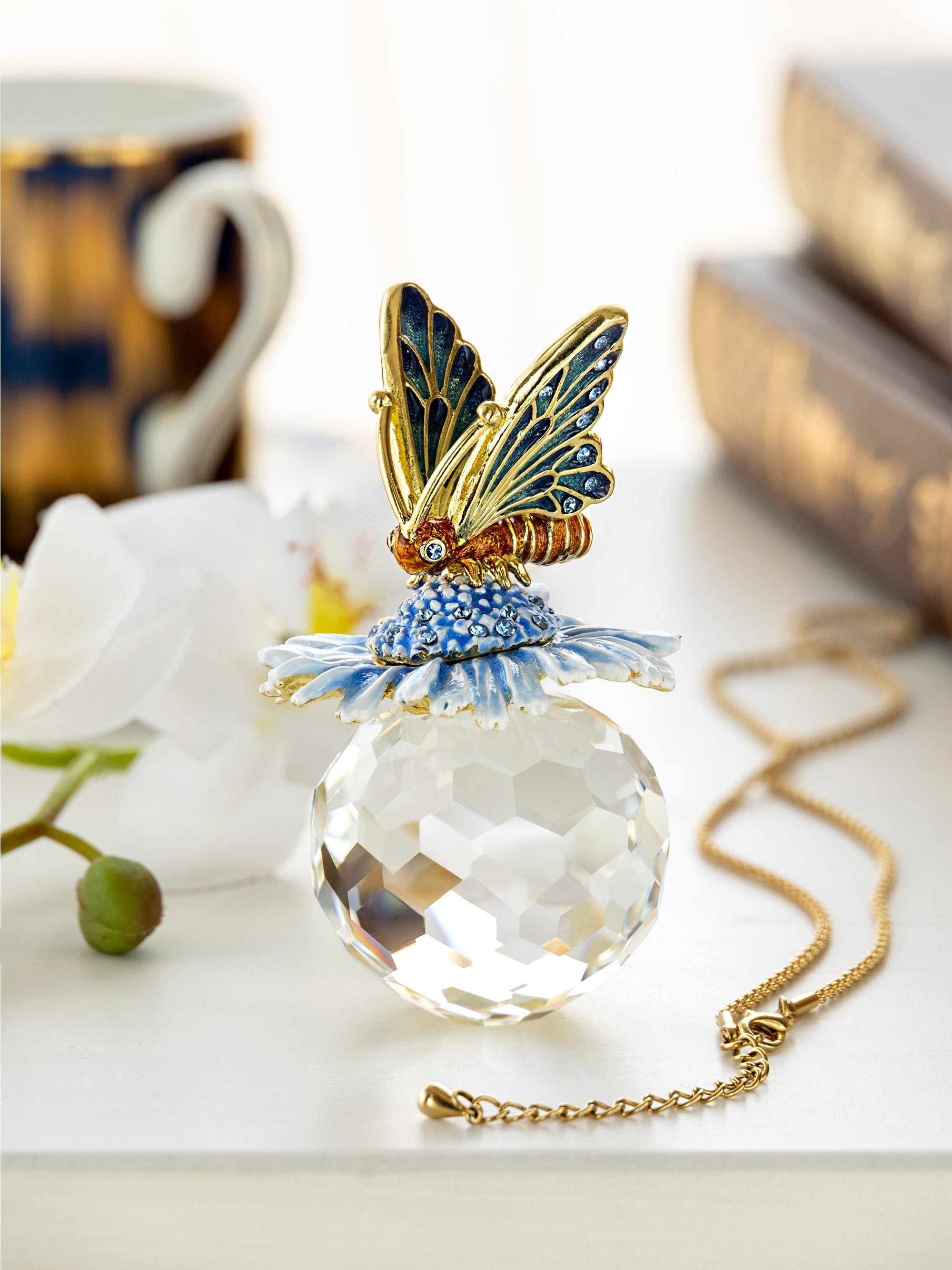 Butterfly-shaped pendant with crystal ball on a chain, placed on a light surface.