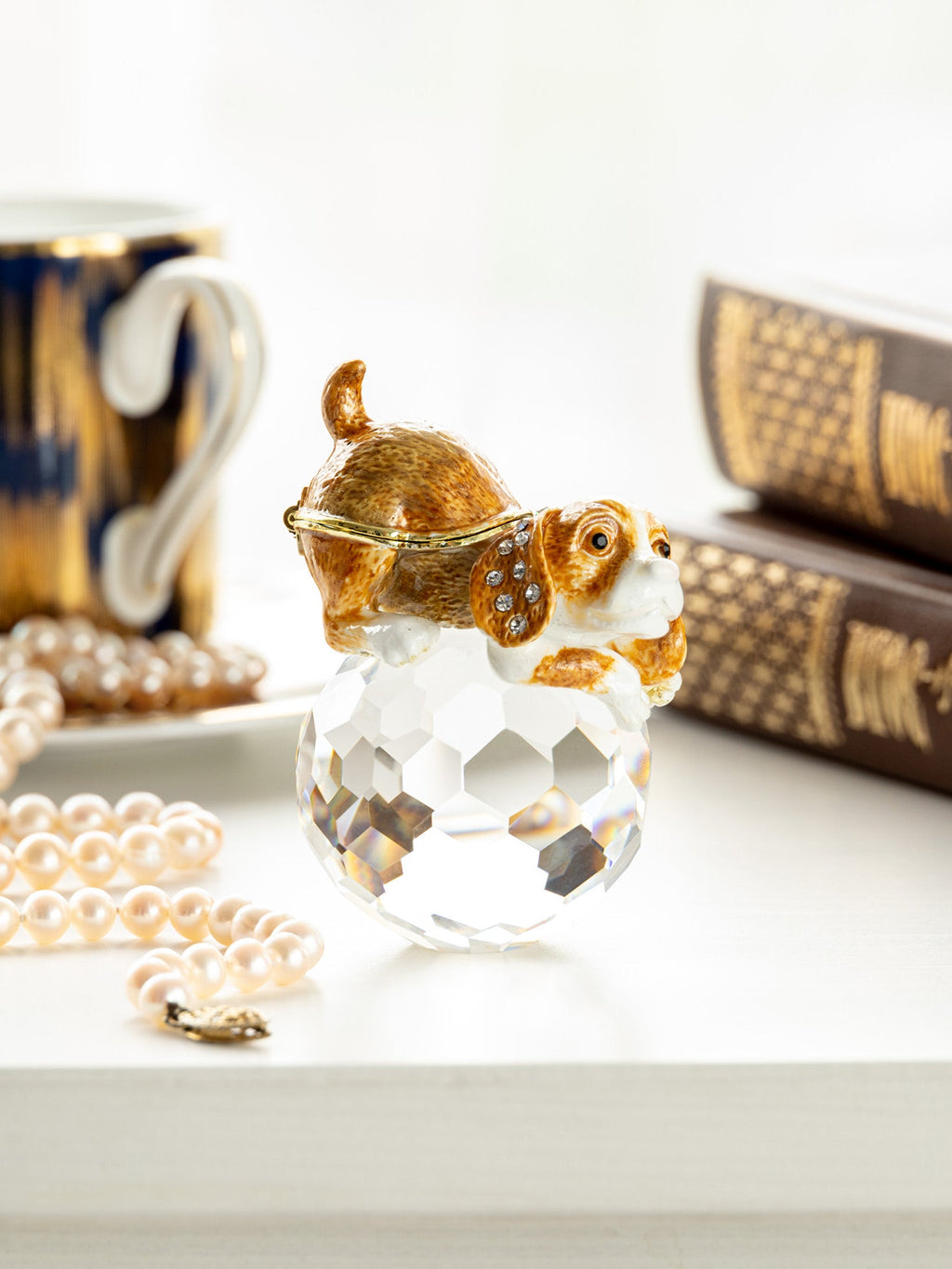 Decorative glass figurine of a dog on a white surface with books and pearls in the background