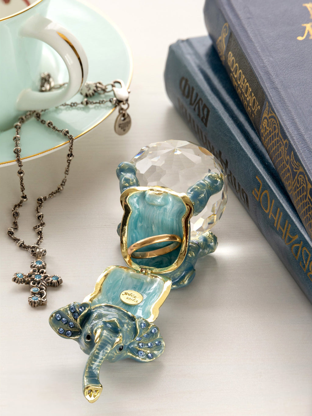Decorative elephant with crystal ball on a white surface next to a teacup and books.
