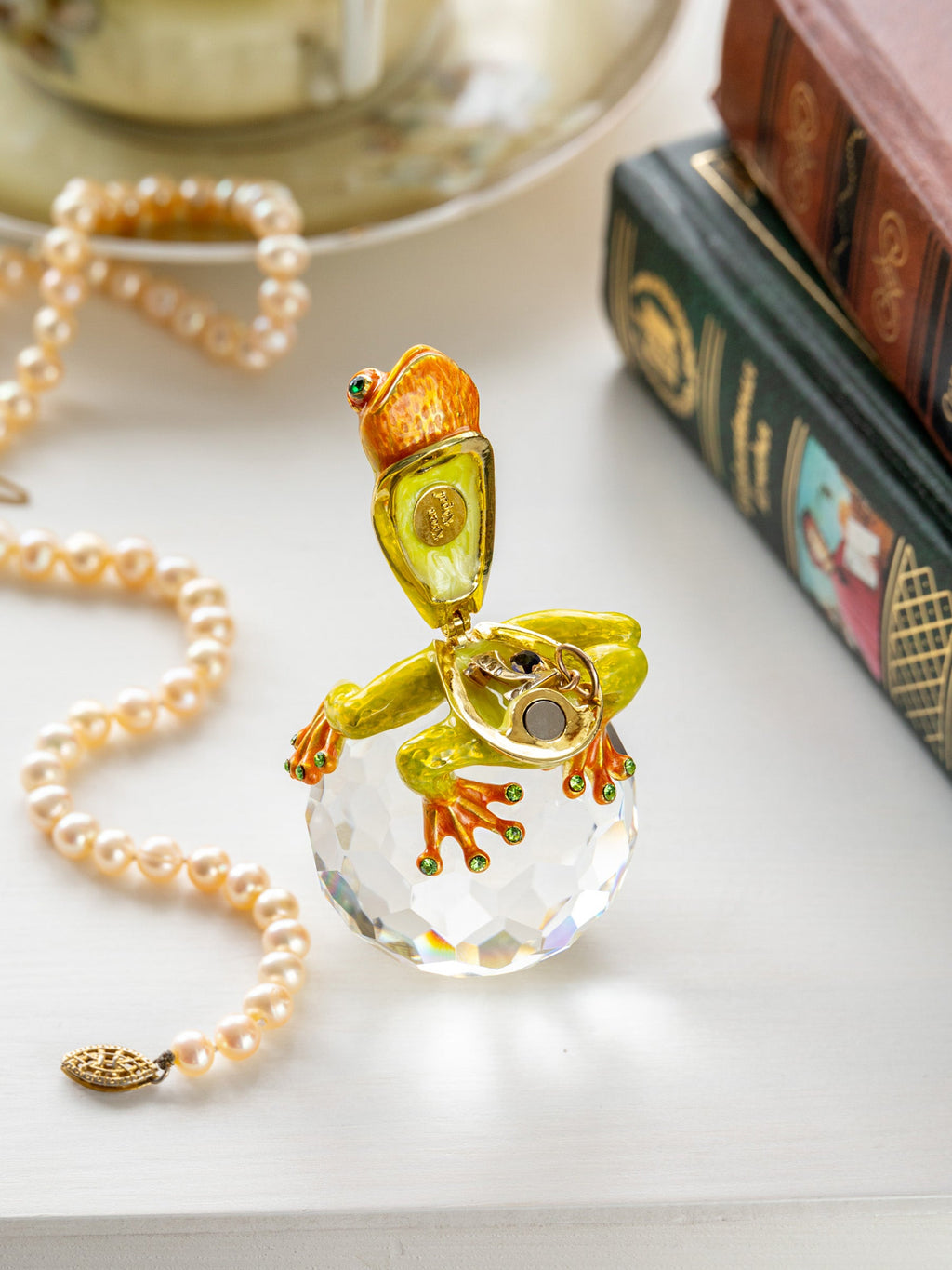 Frog-shaped pendant on a clear crystal ball with a pearl necklace and books in the background.