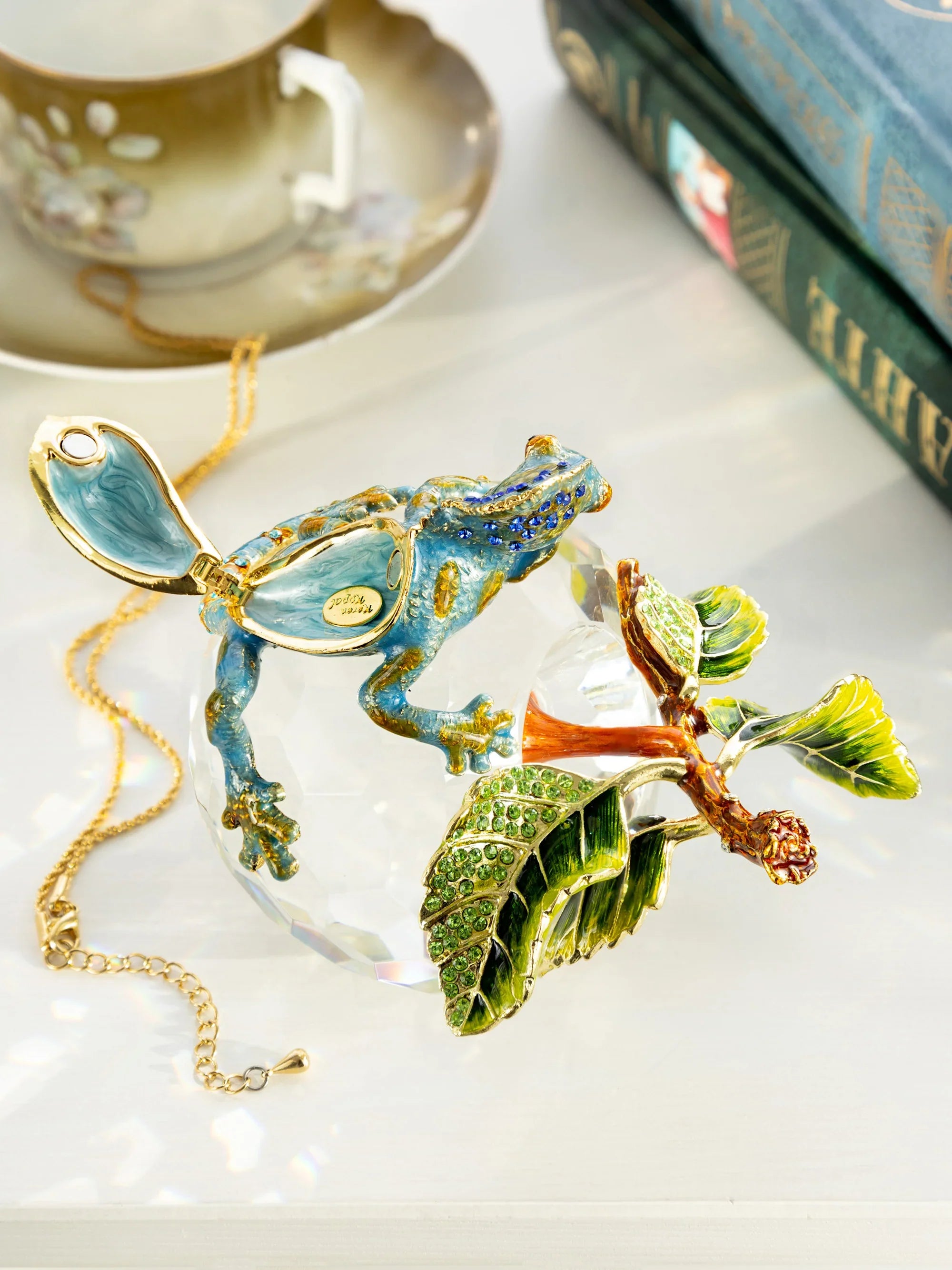 Decorative Chameleon pendant on a chain with a teacup and books in the background