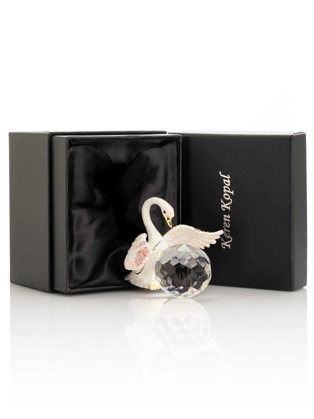 Decorative swan figurine with crystal ball on a white surface, with a black box in the background.