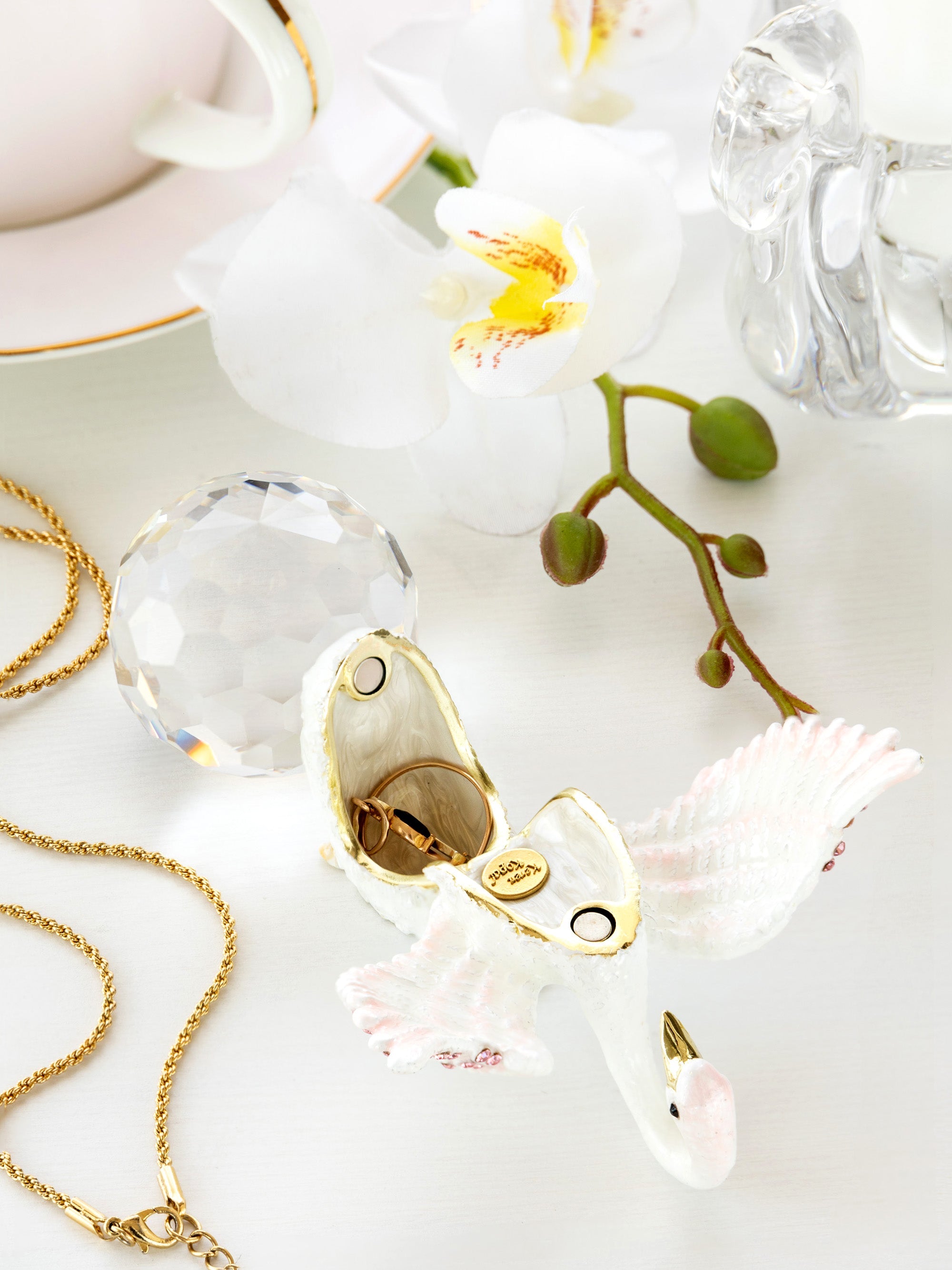 Decorative bird figurine with gold accents on a white surface with flowers and jewelry.