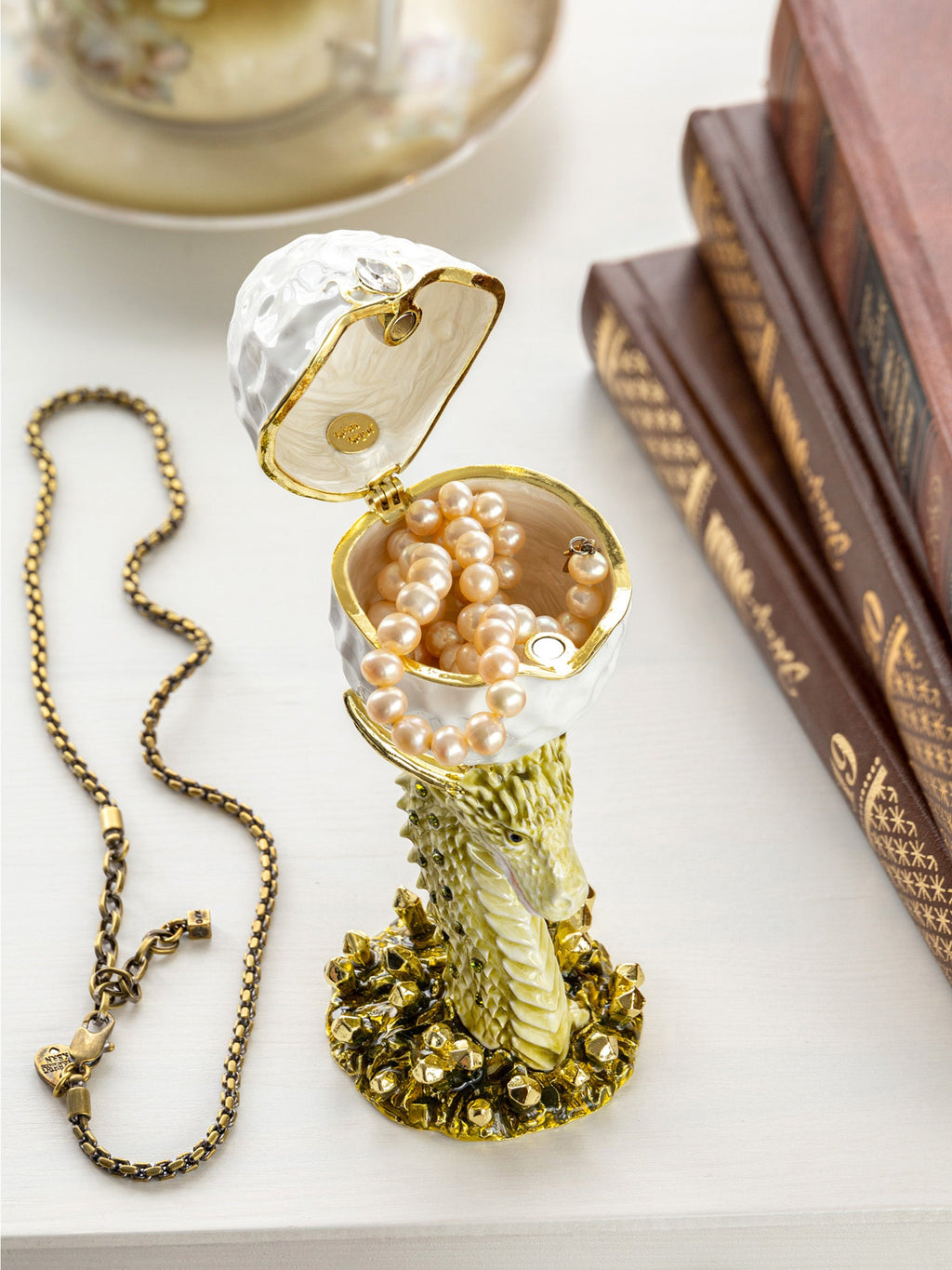 Decorative jewelry box with pearls and a necklace on a surface with books in the background