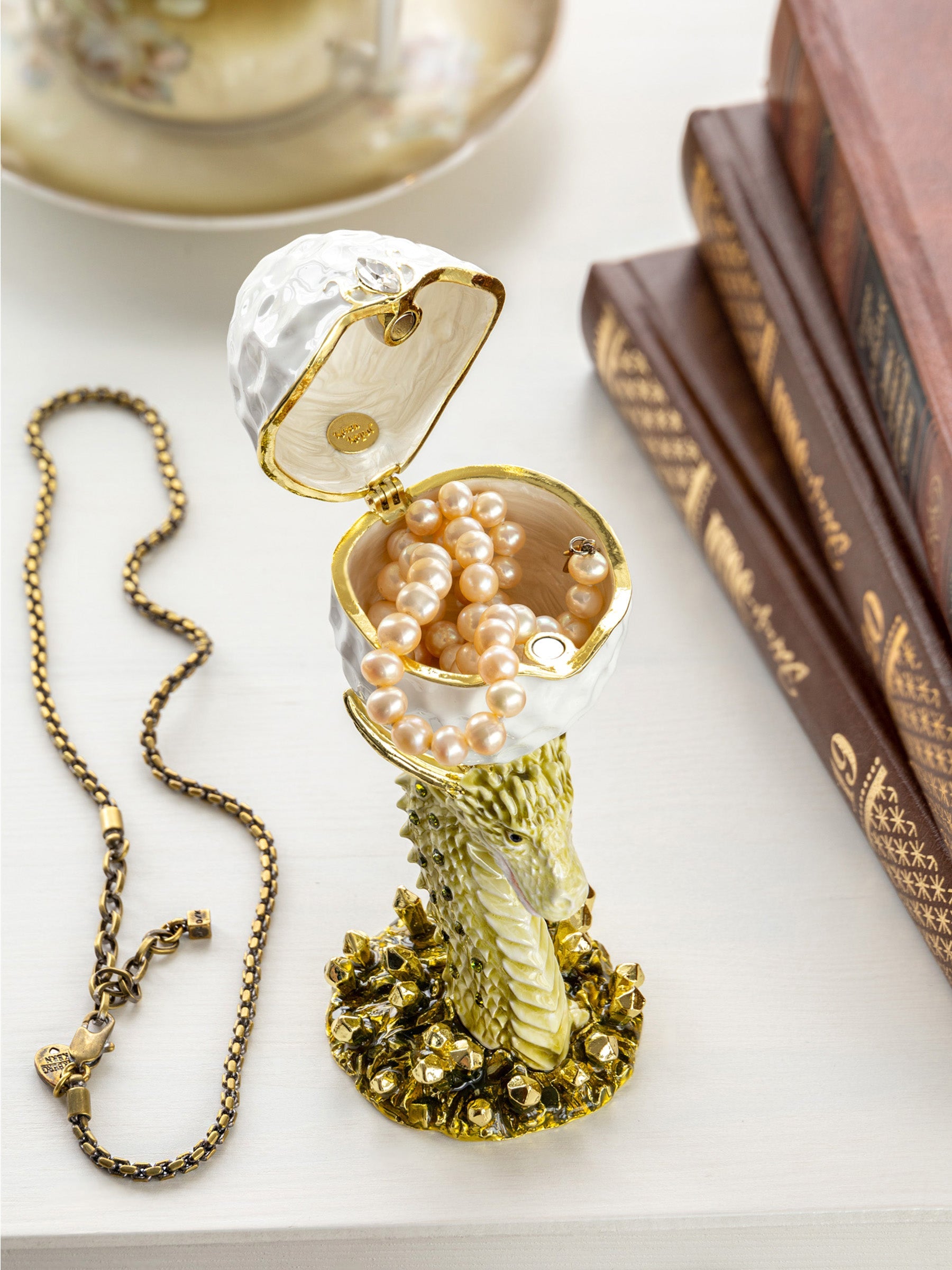 Decorative jewelry box with pearls and a necklace on a surface with books in the background