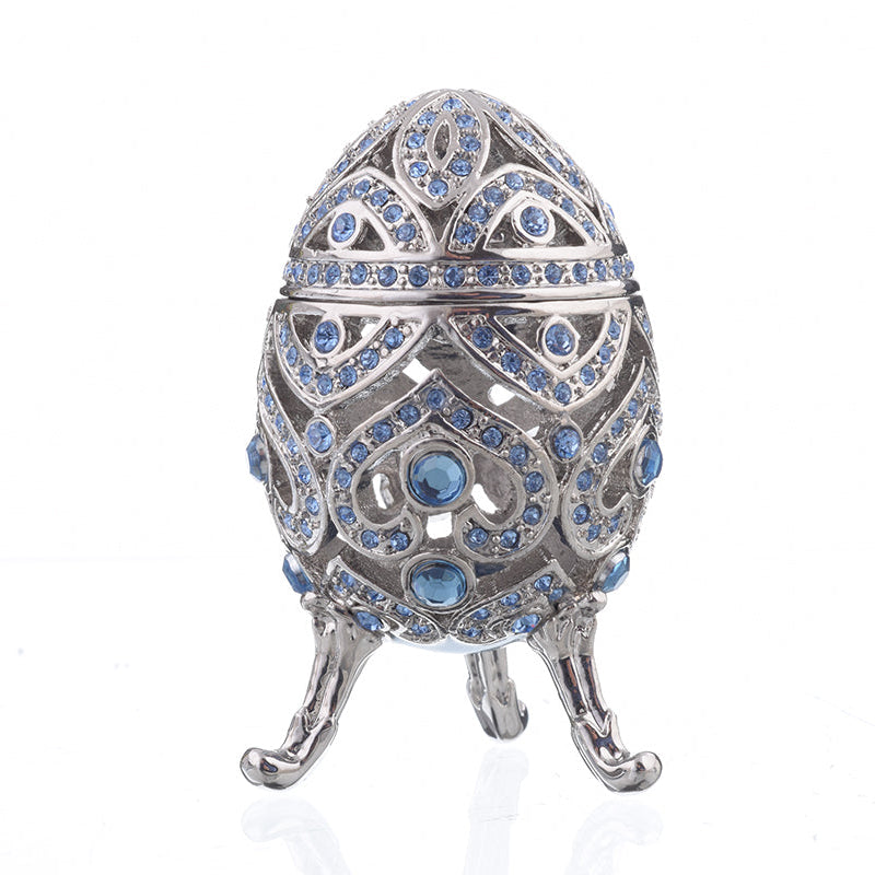 Decorative egg-shaped jewelry box with blue gemstones on a white background