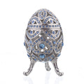 Decorative egg-shaped jewelry box with blue gemstones on a white background