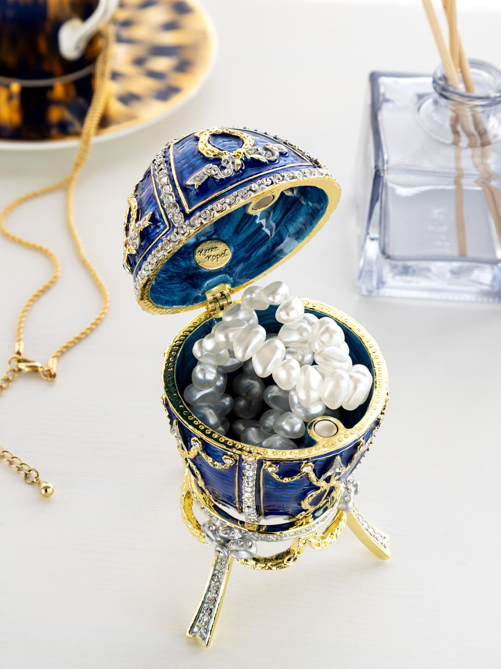 Decorative blue and gold jewelry box with pearls on a white surface