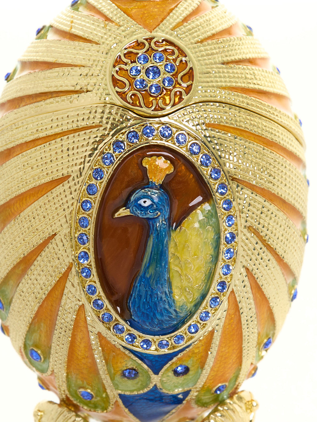 Decorative egg with peacock design and gold embellishments on a white background