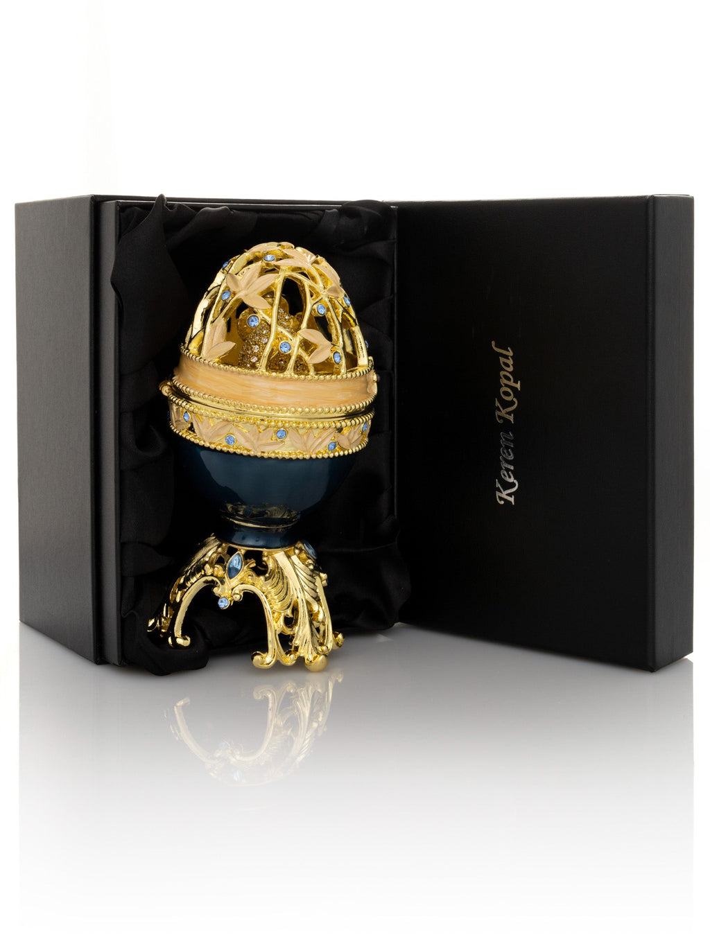 Decorative egg with gold and blue accents on a black stand, branded 'Keren Kopal', against a white background.
