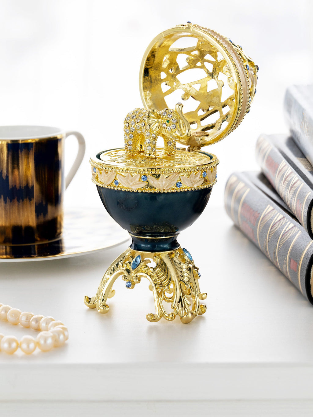 Decorative egg with gold and blue design on a white surface with a cup and books in the background.
