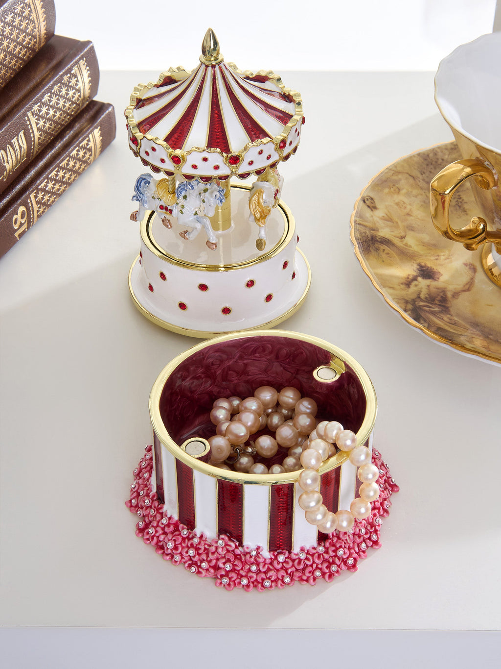 Decorative jewelry box with a carousel design on top, filled with pearls, on a white surface.
