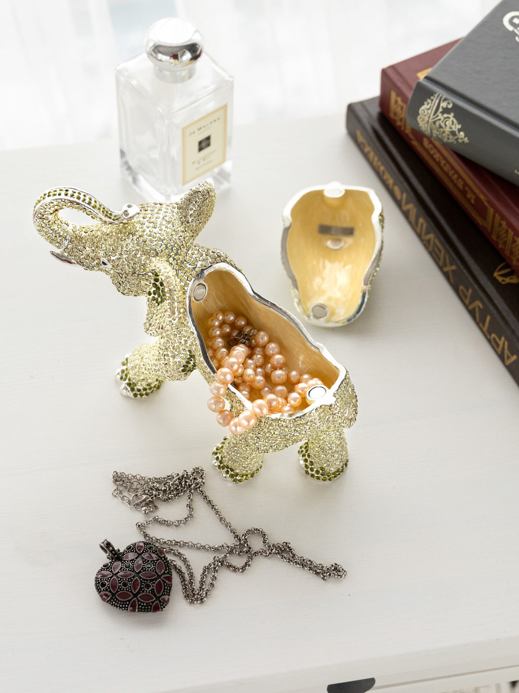 Silver elephant trinket box with pearls and necklace on white surface with books and perfume bottle