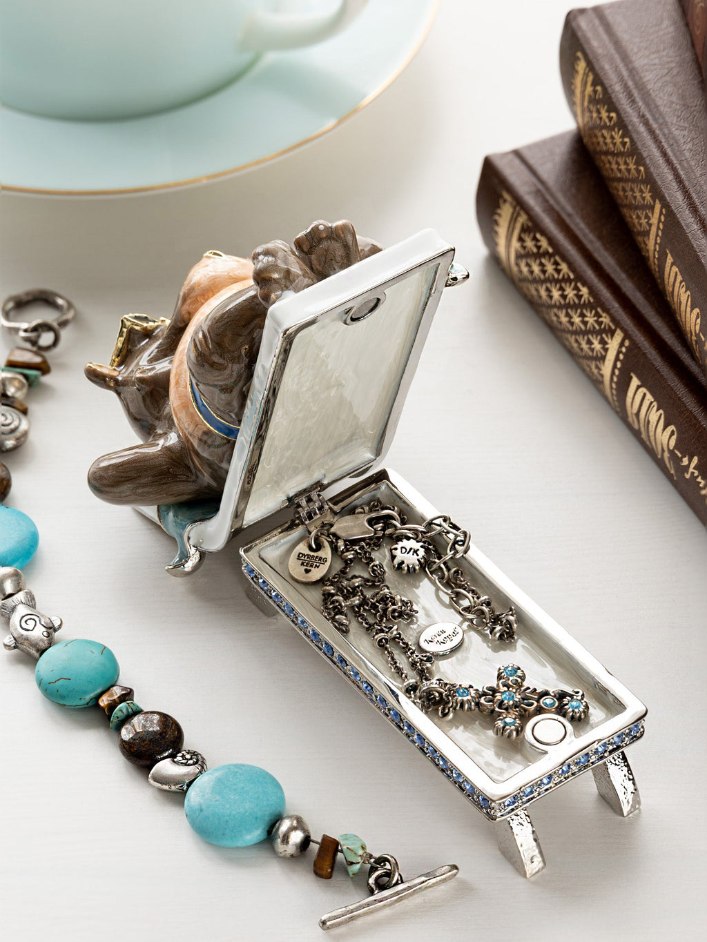 Hippo trinket box opened showing jewelry storage with charms and beads on white surface with books