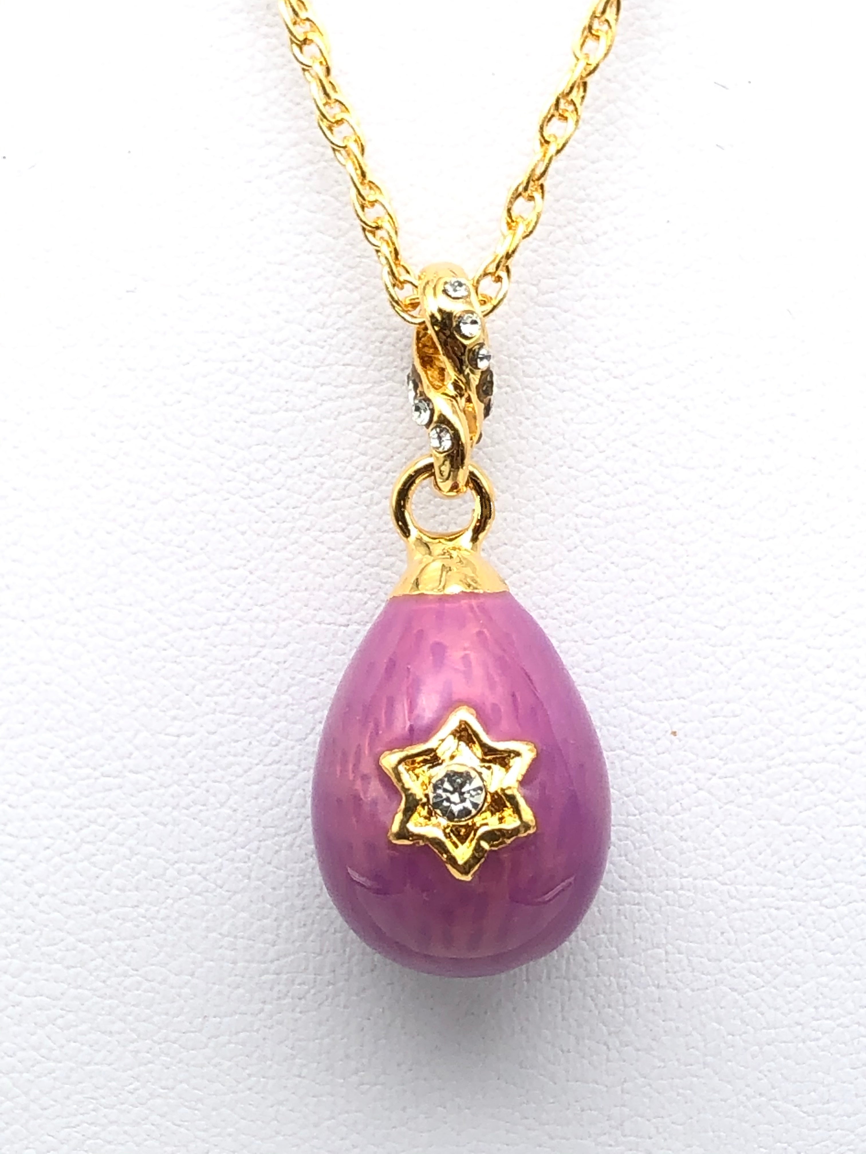 Pink teardrop pendant with gold star design and chain on white background