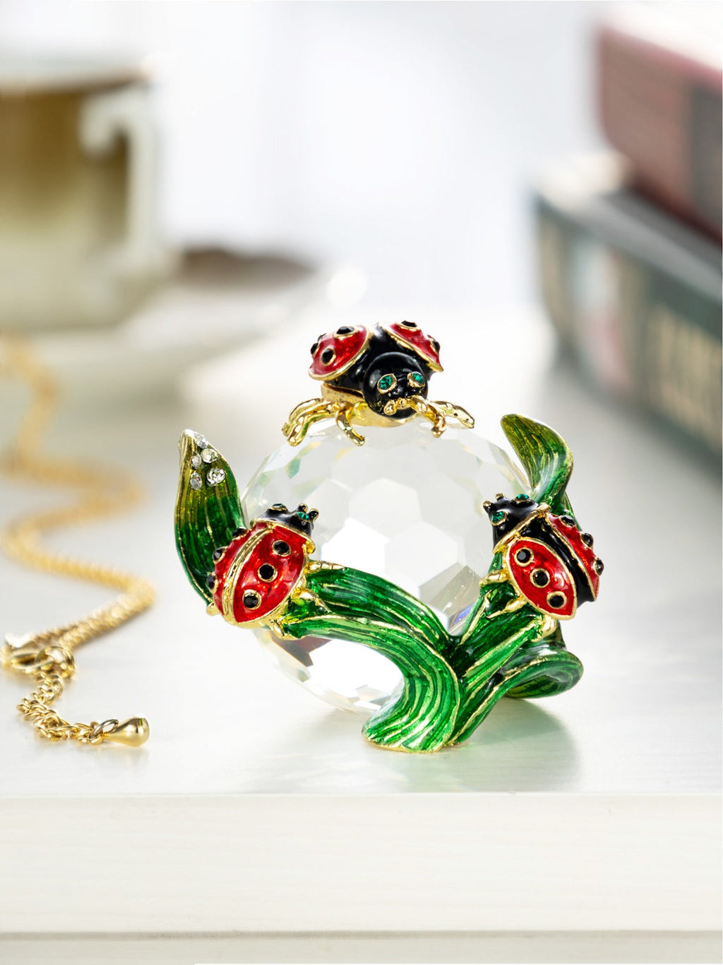 Necklace with a clear crystal pendant featuring green leaves and red ladybug designs on a light background.