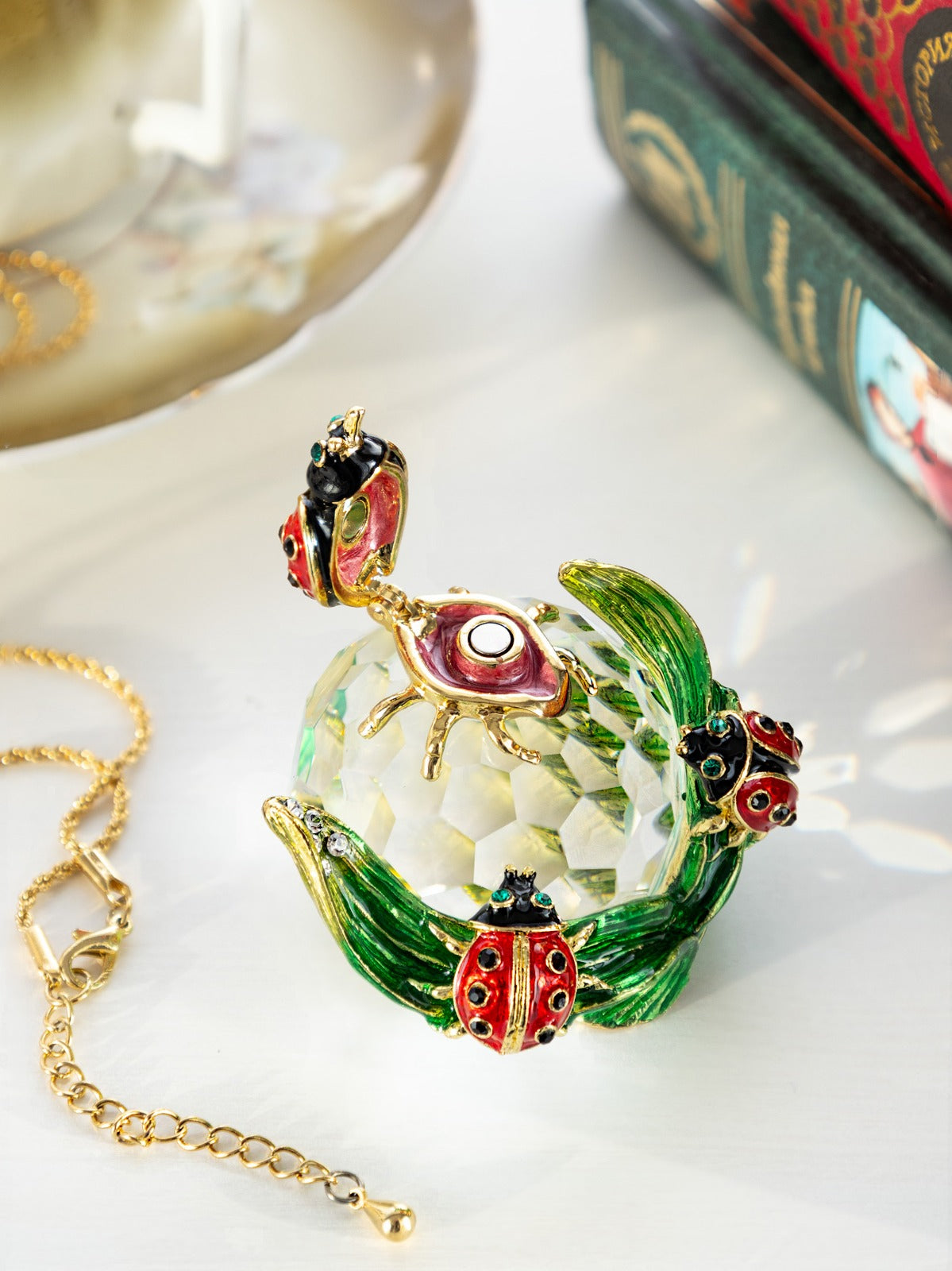 Crystal ball with ladybugs and green leaves on white surface
